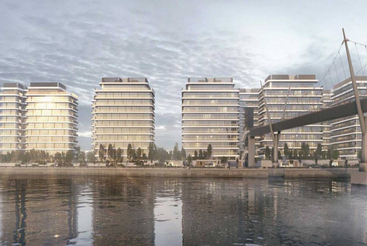 Modern waterfront residential towers with glass facades and pedestrian bridge over calm water